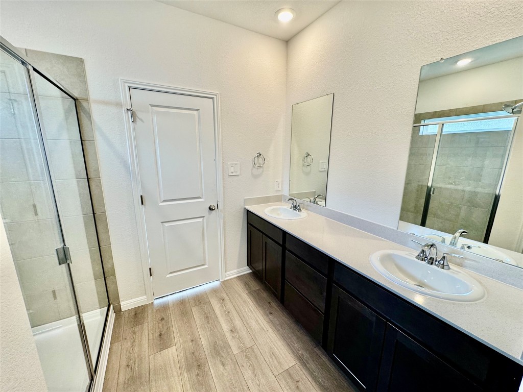133 Boondoggle Ridge Cedar Creek, TX 78612 - Photo 4 of 19 Full bathroom featuring a shower stall, double vanity, light wood-type flooring, and a textured wall