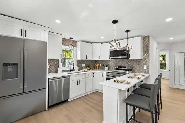 a kitchen with a refrigerator a microwave a stove and white cabinets with wooden floor