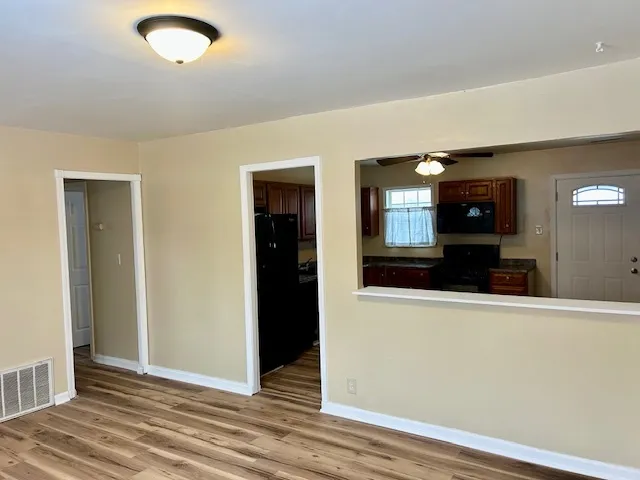 an empty room with wooden floor and way to kitchen