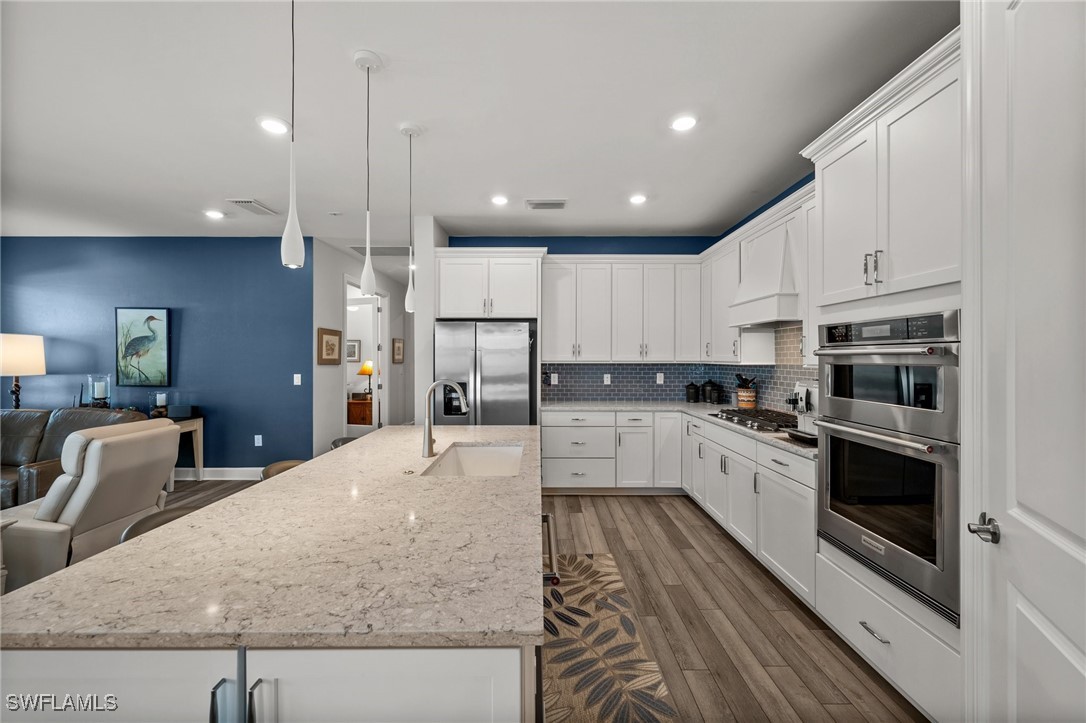 42243 Edgewater Drive Punta Gorda, FL 33982 - Photo 38 of 46 a large kitchen with stainless steel appliances kitchen island granite countertop a stove a sink a refrigerator and white cabinets with wooden floor