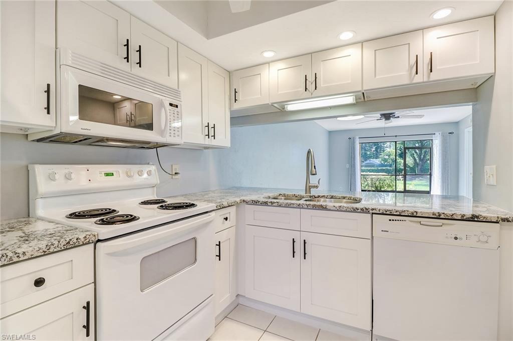5809 Rattlesnake Hammock Road, Unit 102 Naples, FL 34113 - Photo 2 of 23 a kitchen with granite countertop white cabinets and white appliances