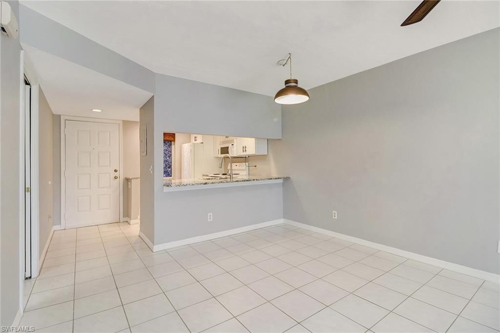 5809 Rattlesnake Hammock Road, Unit 102 Naples, FL 34113 - Photo 4 of 23 an empty room with chandelier fan and kitchen view