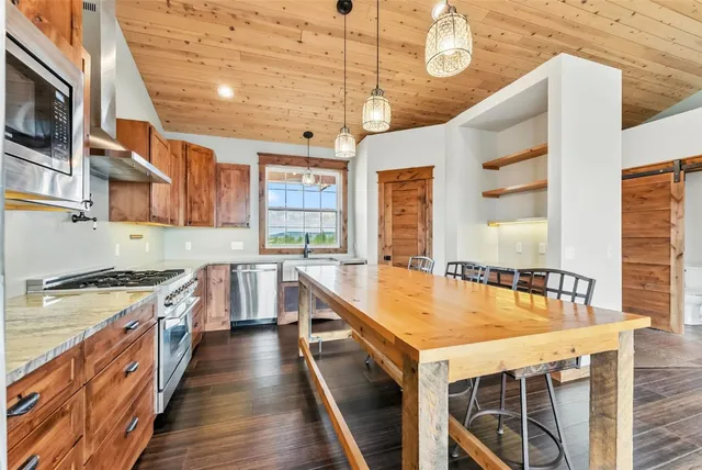 a room with stainless steel appliances kitchen island granite countertop wooden floor and a view of living room