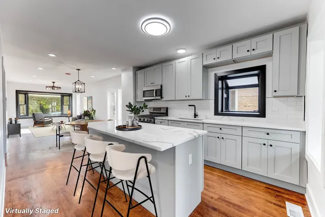 a kitchen with stainless steel appliances granite countertop a stove top oven a sink a dining table and chairs with wooden floor