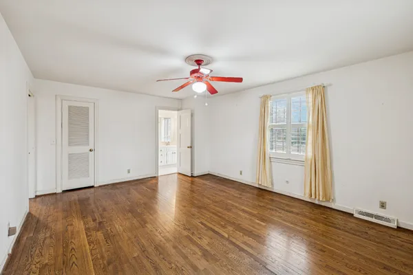 a view of an empty room with wooden floor and a ceiling fan