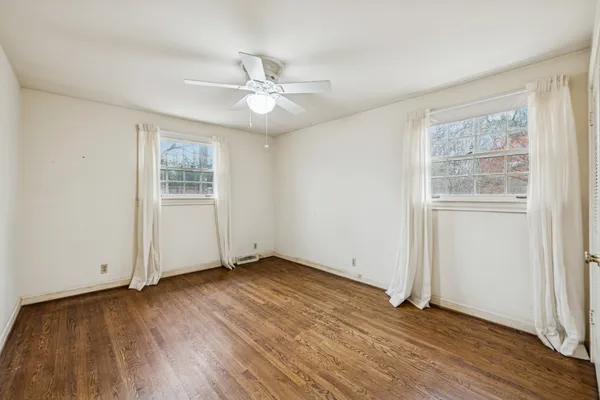an empty room with wooden floor chandelier fan and windows