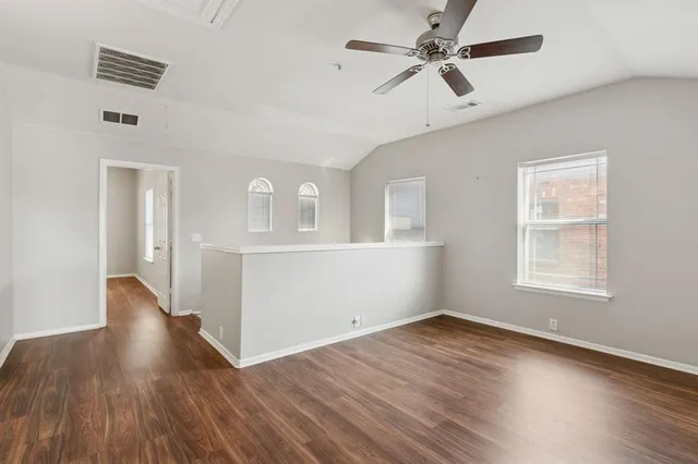 an empty room with wooden floor chandelier fan and windows