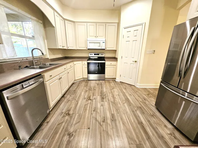 a kitchen with stainless steel appliances wooden floor sink and a window