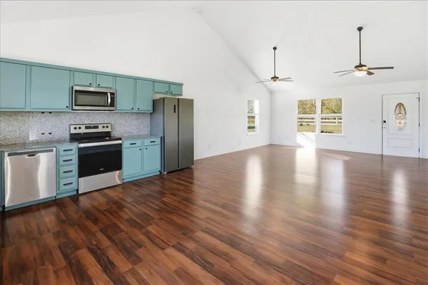 a view of a kitchen with stainless steel appliances granite countertop a stove top oven a refrigerator with wooden floors and a fireplace