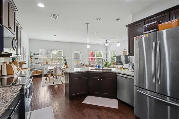 a kitchen with stainless steel appliances granite countertop a refrigerator a sink dishwasher a stove and a dining table with wooden floor