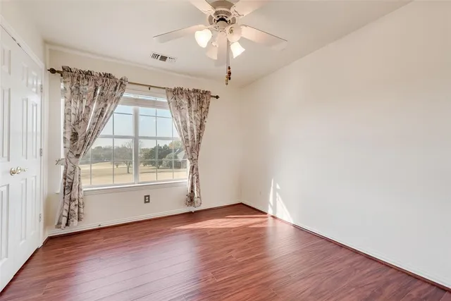 an empty room with wooden floor fan and windows