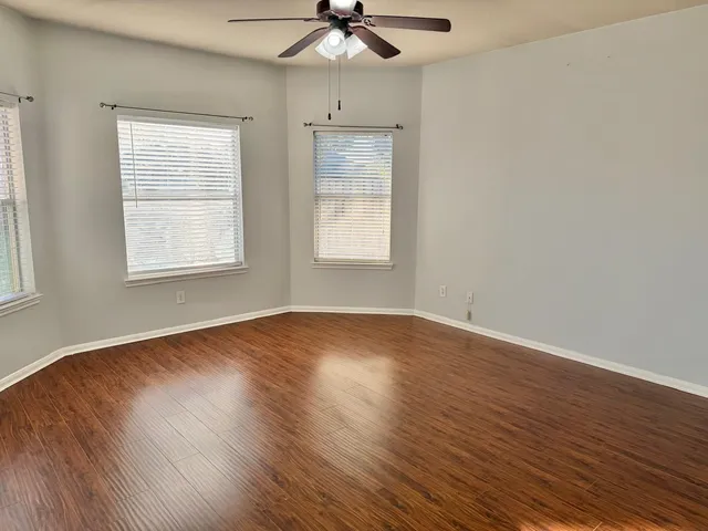 an empty room with wooden floor chandelier fan and windows