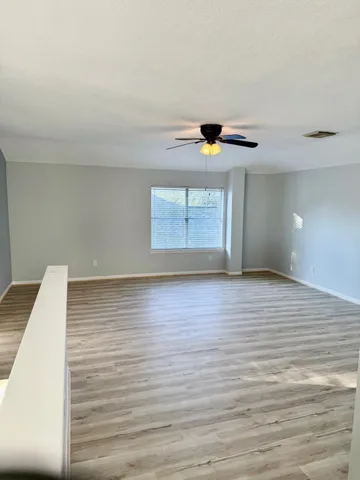 an empty room with wooden floor fan and windows