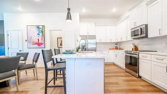 a kitchen with stainless steel appliances kitchen island granite countertop a stove top oven a sink a dining table and chairs with wooden floor