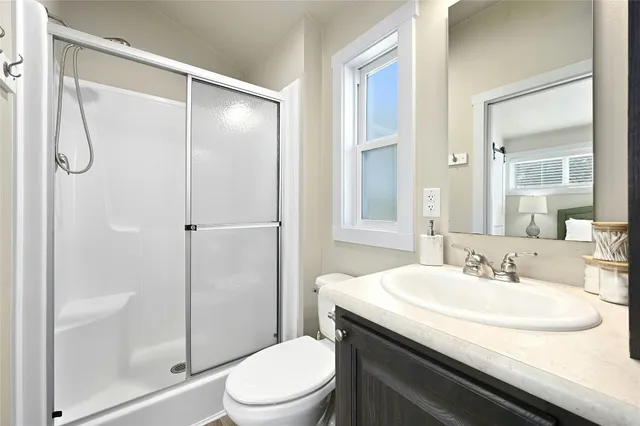 a bedroom with a bed and a lamp on dresser with wooden floor