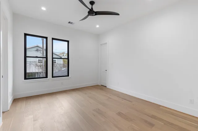 an empty room with wooden floor chandelier fan and windows