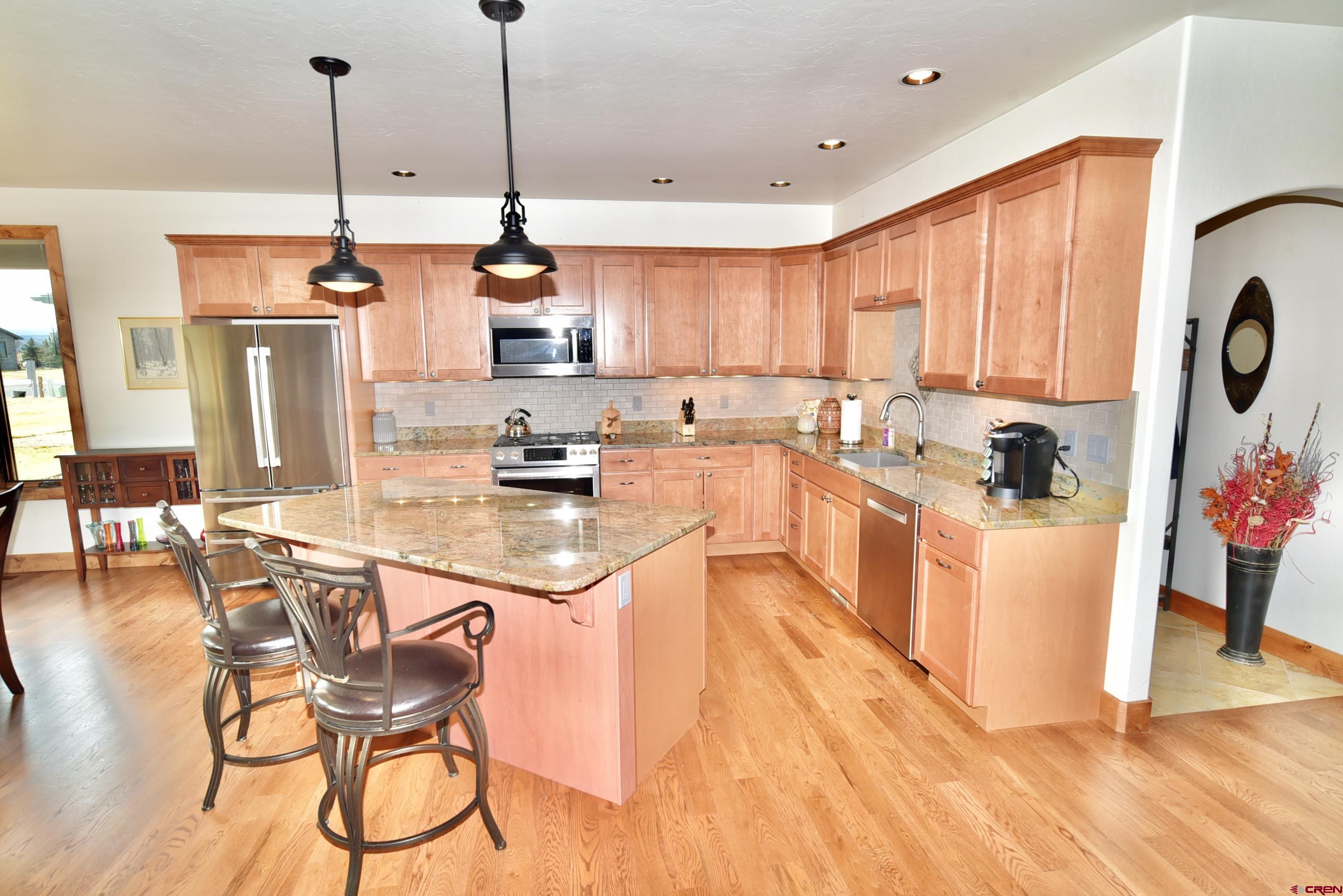 2136 Signature Ridge Lane Montrose, CO 81401 - Photo 14 of 32 a kitchen with stainless steel appliances kitchen island granite countertop a sink a stove a refrigerator and white cabinets with wooden floor