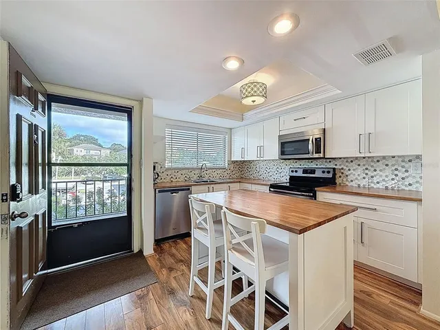 a kitchen with stainless steel appliances granite countertop a stove top oven a sink dishwasher a refrigerator and white cabinets with wooden floor