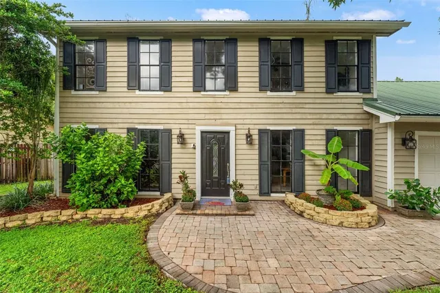 a view of a house with small yard plants and large tree