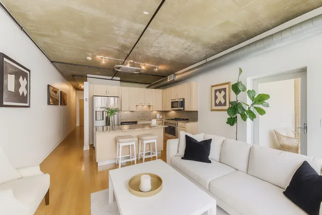 a living room with stainless steel appliances furniture a rug and a kitchen view