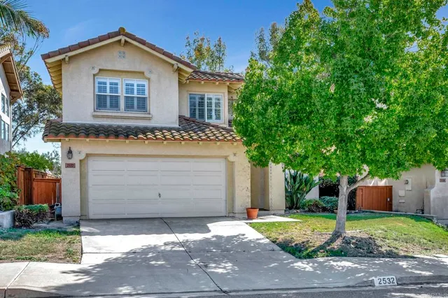 a view of a house with a yard plants and large tree