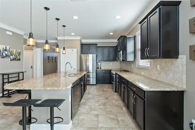 a kitchen with stainless steel appliances granite countertop a sink a stove a refrigerator and chairs