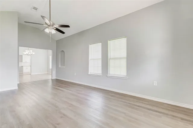 an empty room with wooden floor chandelier fan and windows