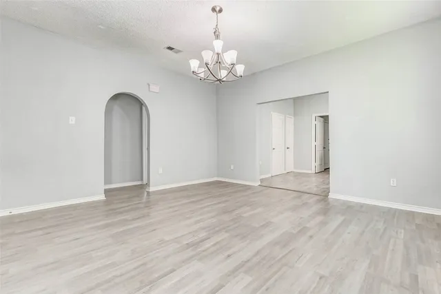 a view of an empty room with chandelier and wooden floor