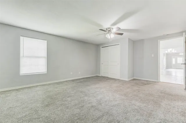 an empty room with chandelier fan and windows