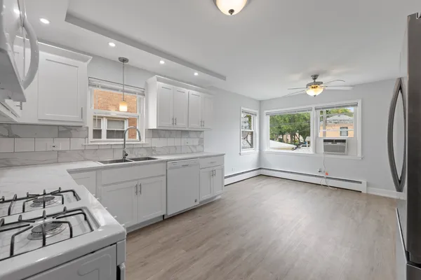 a kitchen with granite countertop a stove a sink and white cabinets with wooden floor next to windows