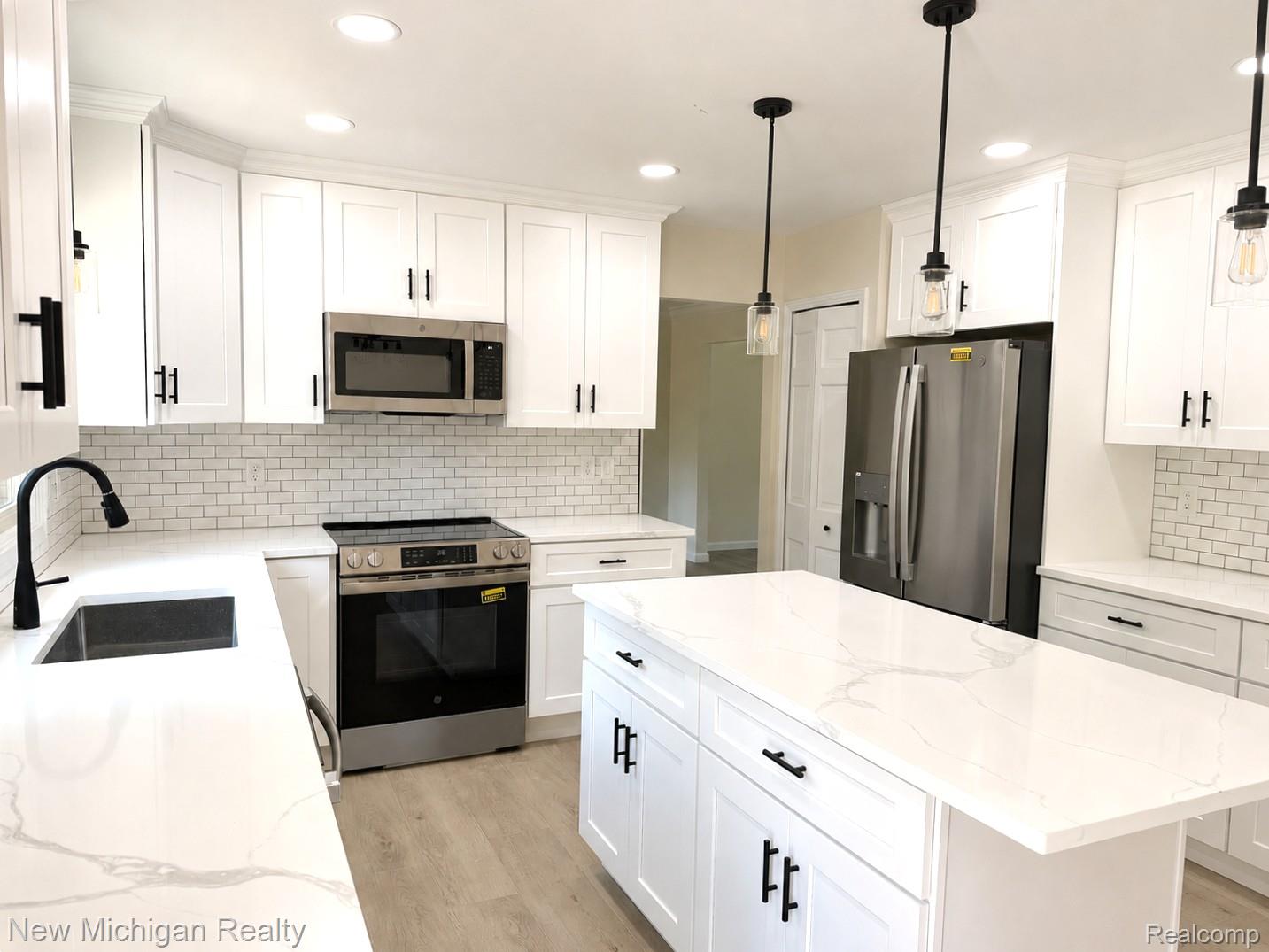 Bright kitchen featuring new cabinetry, stainless steel appliances, a subway tile backsplash, light wood-finish flooring, and a central island with Quartz countertop