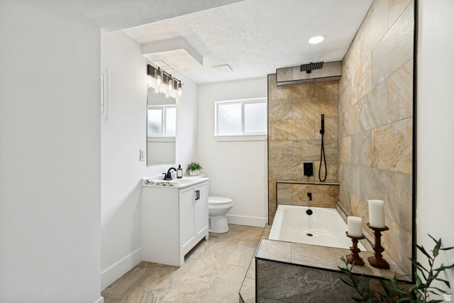62 South Clark Lane Elk Ridge, UT 84651 - Photo 22 of 30 Bathroom featuring a soaking tub with integrated tiled surround, large format stone-finish wall tiling, a rainfall shower fixture, and a white vanity with a dark countertop and black hardware
