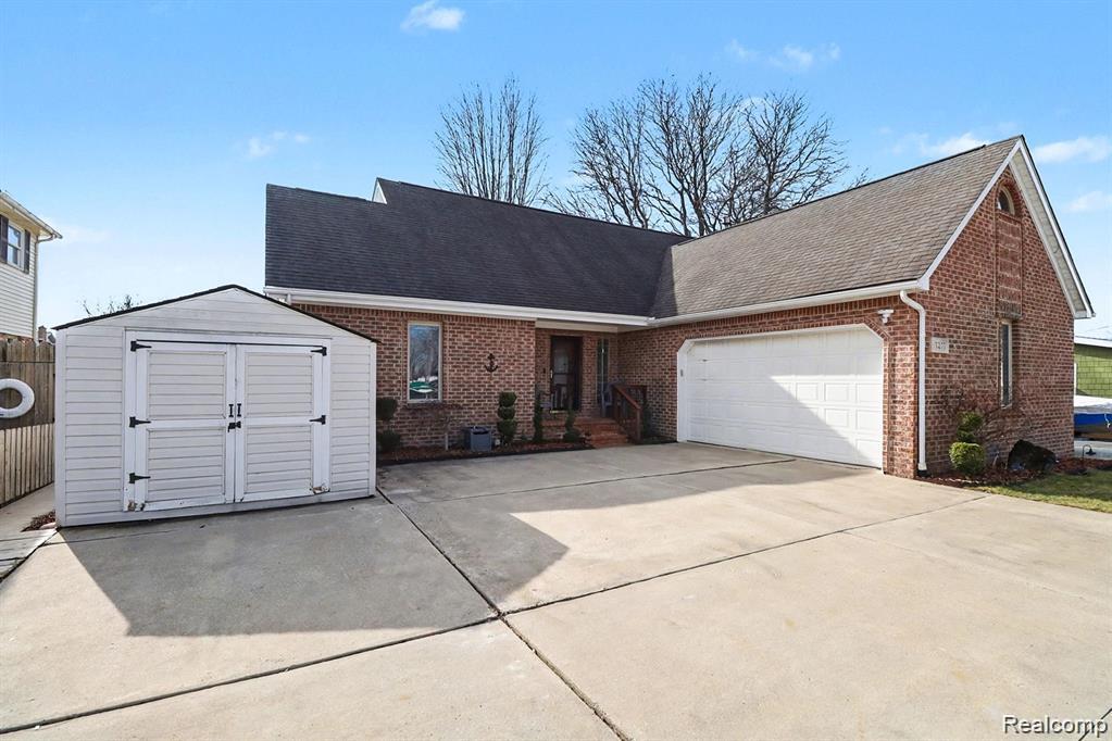View of front of property with brick siding, an attached garage, a storage unit, and concrete driveway