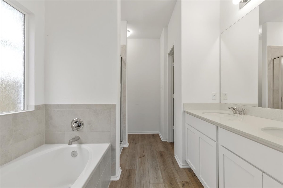 101 Rowdy Yates Way Jarrell, TX 76537 - Photo 18 of 32 Bathroom featuring a white soaking tub with light gray tile surround, double vanity with white cabinetry and light-colored countertops, polished chrome fixtures, and wood-finish flooring