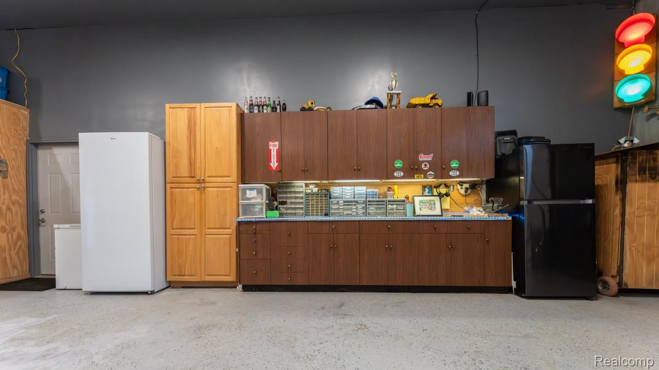 2418 South 41st Road South Cadillac, MI 49601 - Photo 25 of 57 Spacious utility area featuring dark cabinetry with integrated task lighting, a light wood-finish pantry, a white entry door, and concrete flooring