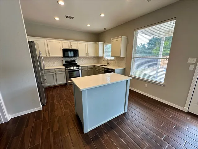 a large kitchen with stainless steel appliances wooden floors and a large window