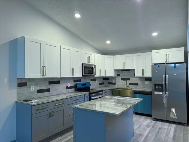 a kitchen with stainless steel appliances granite countertop a stove top oven a refrigerator a sink and dishwasher with wooden floor