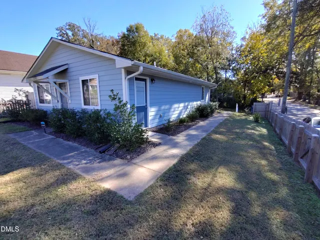 a view of a yard in front of a house with plants and large tree
