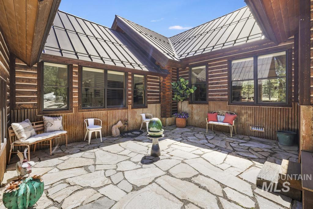 65 Goat Creek Way Stanley, ID 83278 - Photo 3 of 32 Expansive flagstone patio area featuring a metal roof, log siding, multiple windows with dark frames, and wood-paneled walls