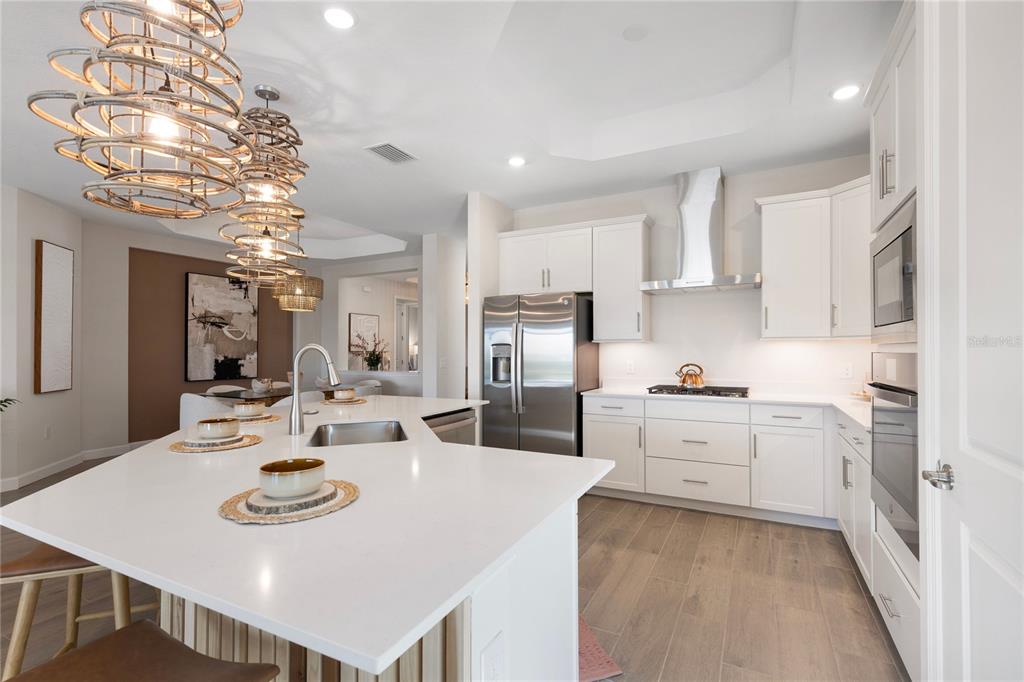 7157 Inlet Isles Lakewood Ranch, FL 34202 - Photo 3 of 26 a kitchen with stainless steel appliances kitchen island granite countertop a sink a stove a refrigerator and a dining table with wooden floor
