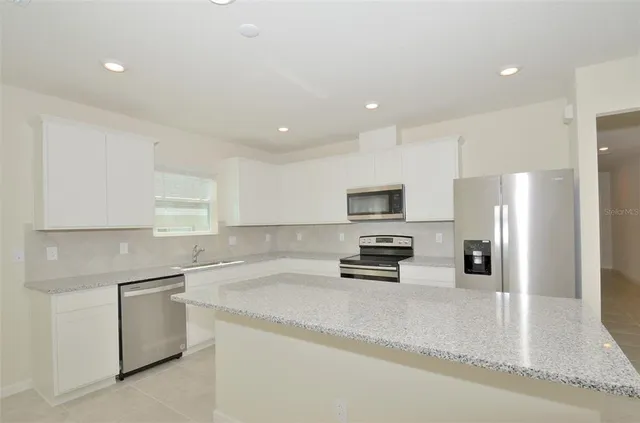 a large white kitchen with kitchen island a stove a sink a refrigerator and white cabinets with wooden floor