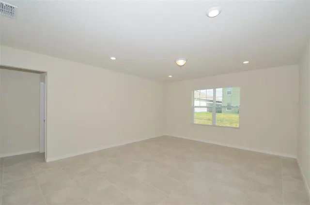an empty room with windows and view of kitchen