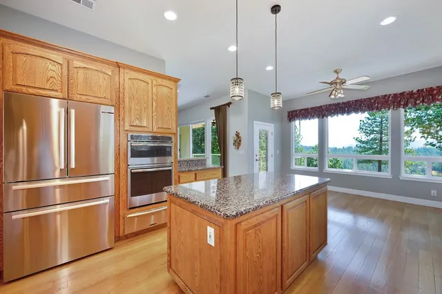 a kitchen with stainless steel appliances granite countertop a refrigerator a oven and a sink with wooden floor