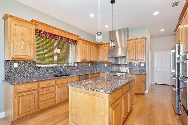 a kitchen with stainless steel appliances granite countertop a sink a stove and a wooden floors