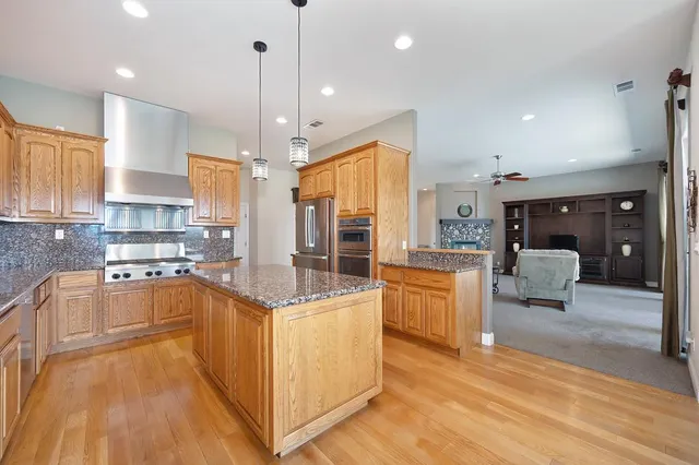 a kitchen with stainless steel appliances granite countertop a stove top oven a refrigerator a sink and white cabinets with wooden floor