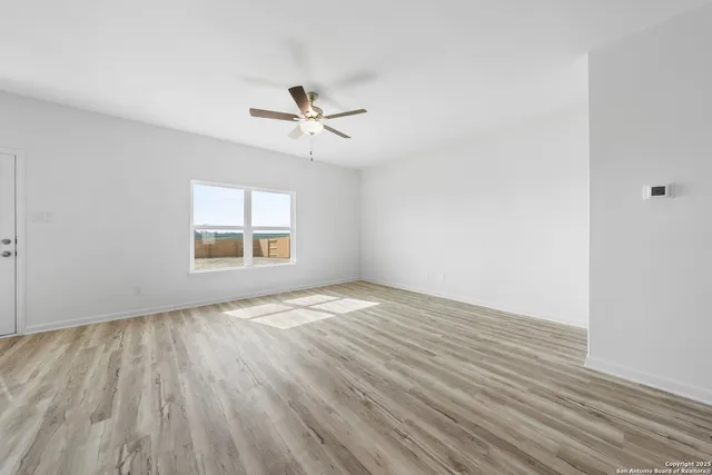 an empty room with wooden floor ceiling fan and window