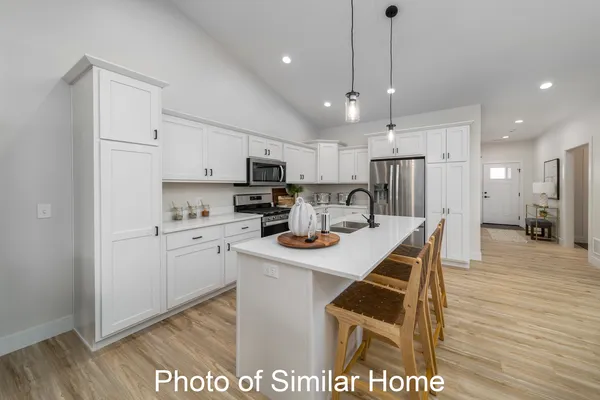 a kitchen with stainless steel appliances granite countertop a sink a stove a refrigerator and white cabinets with wooden floor