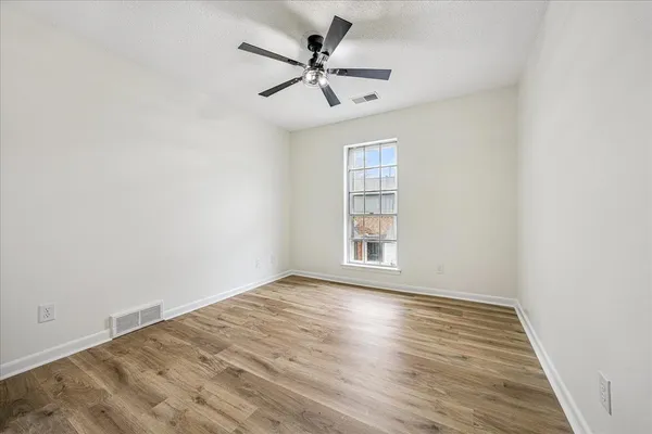 an empty room with wooden floor fan and windows
