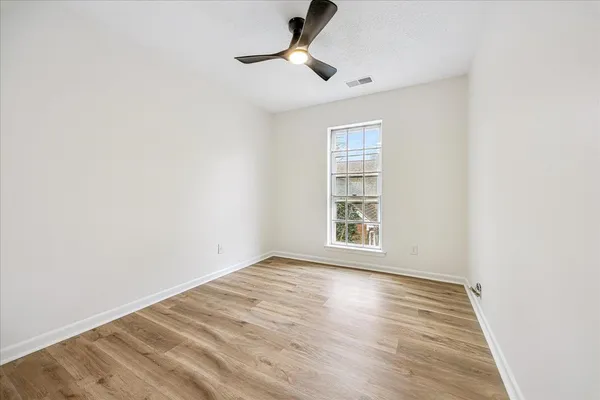 an empty room with wooden floor chandelier fan and windows