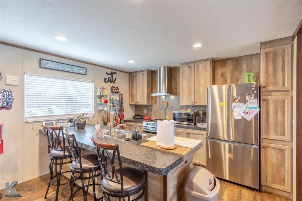 1301 Roma Lane Abilene, TX 79603 - Photo 5 of 20 Kitchen featuring appliances with stainless steel finishes, wall chimney range hood, wood finished floors, dark countertops, and recessed lighting